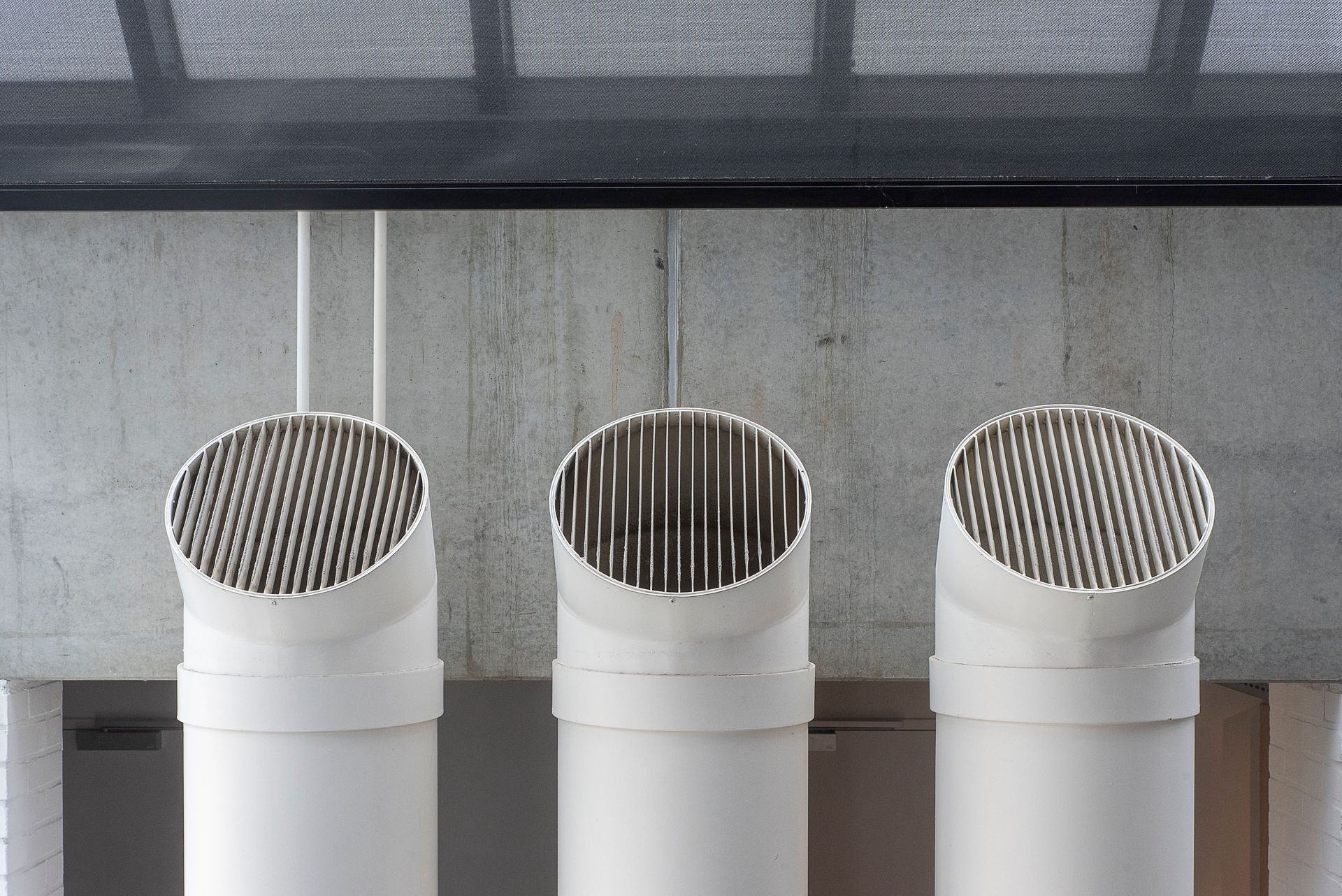 Three white industrial ventilation pipes aligned on concrete wall.